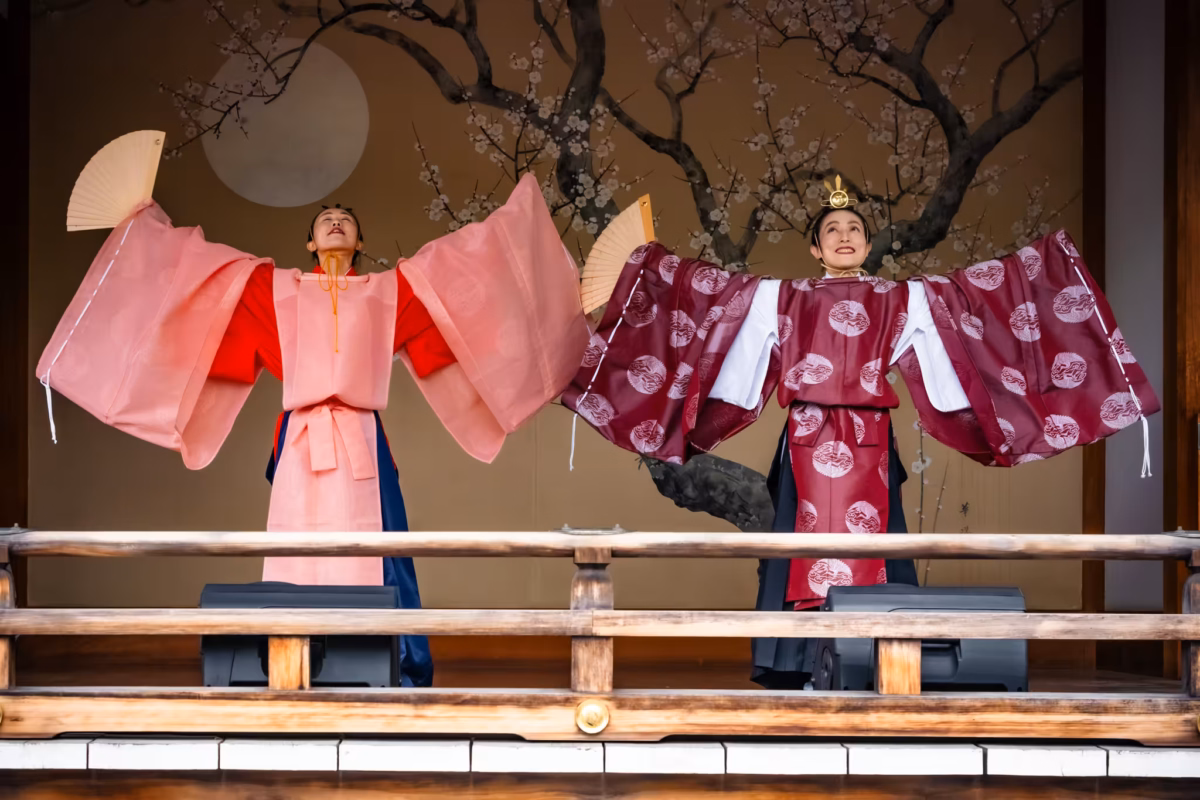 Two miko in chihaya with arms extended stand on a kaguraden.