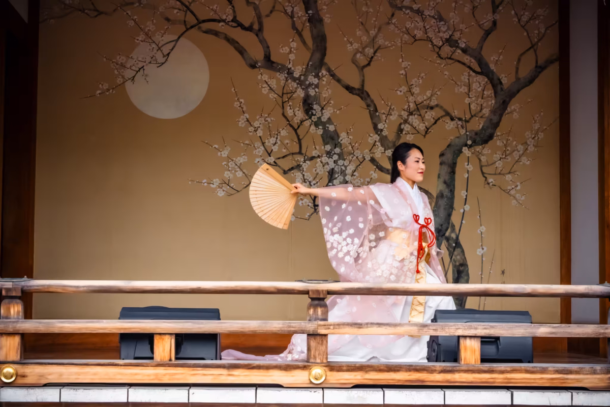 A Miko dances on a Kaguraden extending a fan behind her.
