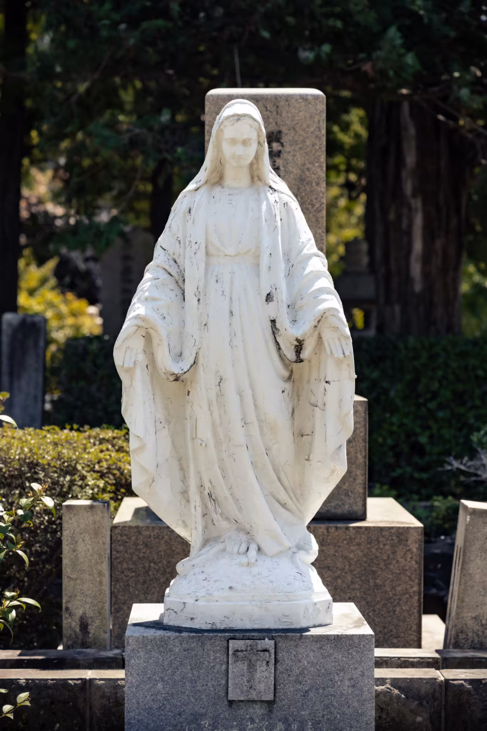 A white Mother Mary statue in a cemetery.