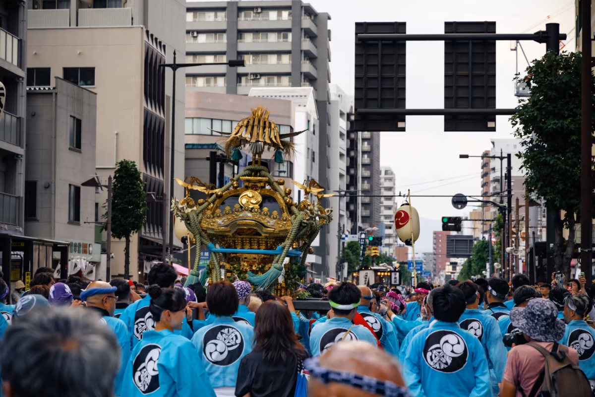 People in blue happi coats walk next to a festival mikoshi.