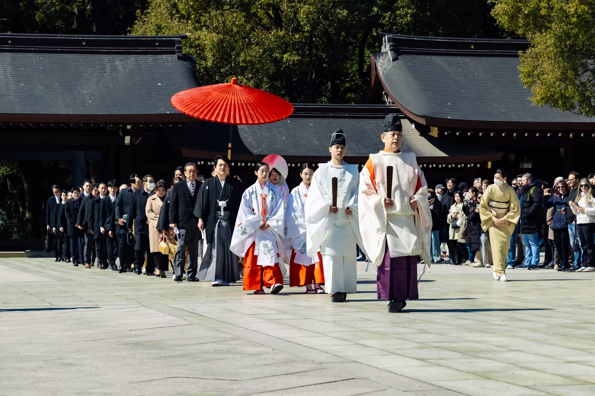 Shinto priests and miko lead a wedding procession across the courtyard of Meiji Shrine.