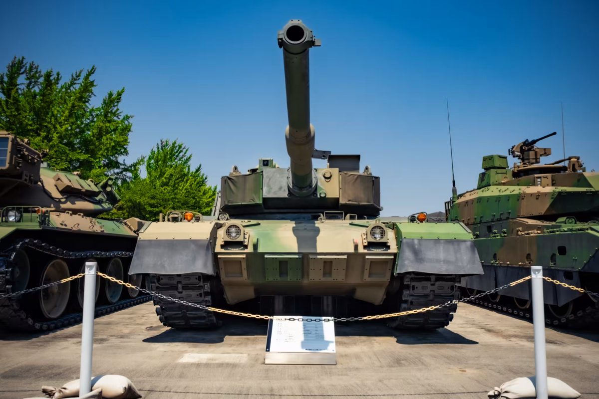 A display Type 90 tank sits outside under a blue sky.