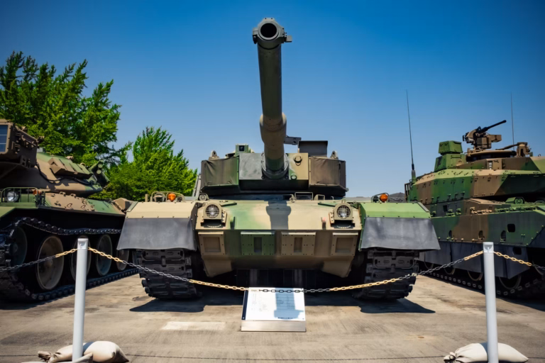 A display Type 90 tank sits outside under a blue sky.