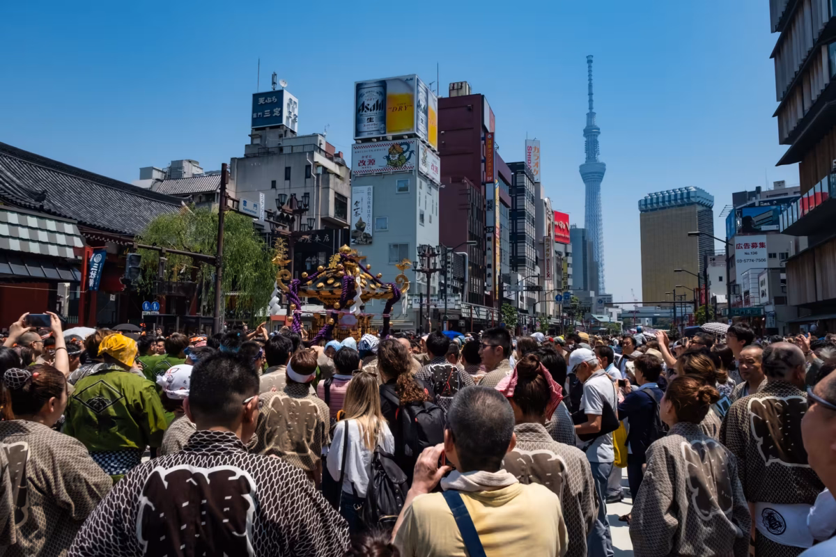 A huge crowd of Sanja Matsuri supporters carry a mikoshi with Tokyo Skytree in the background.