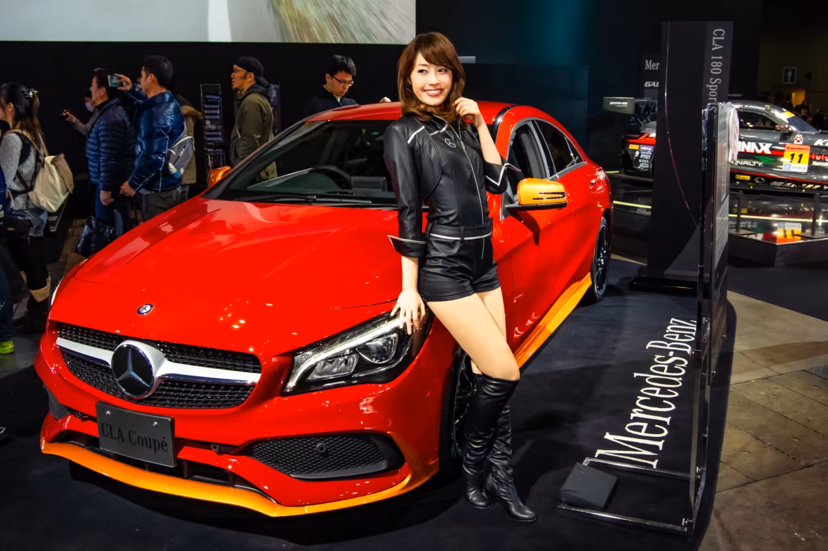 A model clad in leather poses next to a red Mercedes.