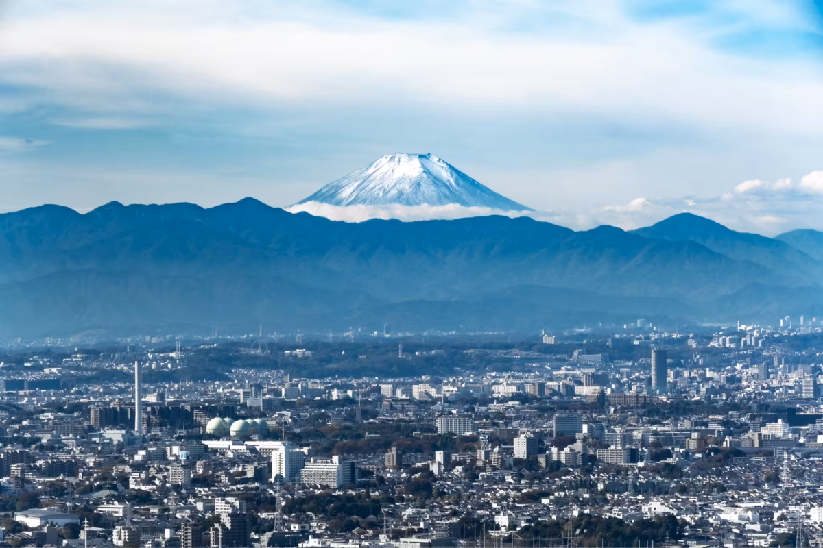 A snow-capped Mount Fuji stands behind a city.