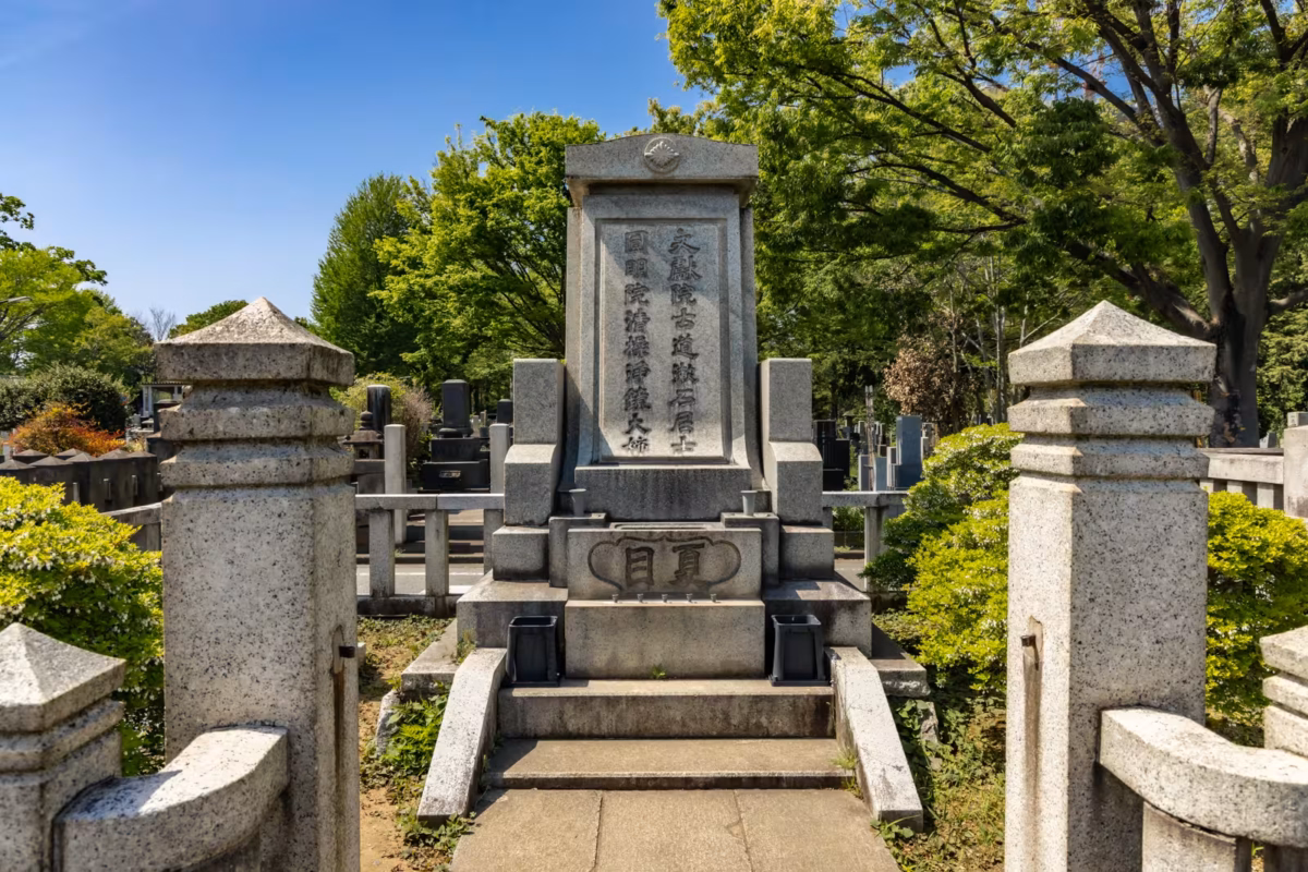 The grave of Natsume Soseki sits in an enclosure with trees in the background.