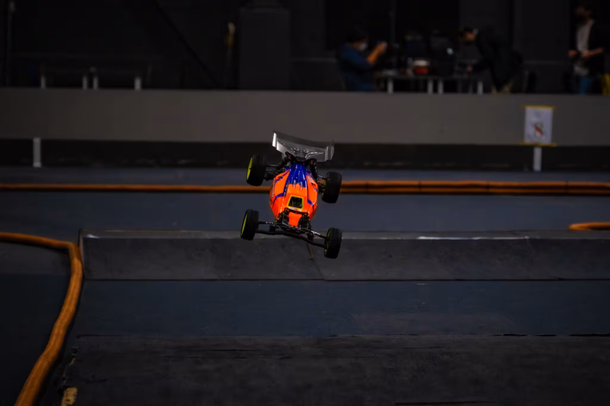 An orange RC car flies over a jump at Tsukuba RC Arena.