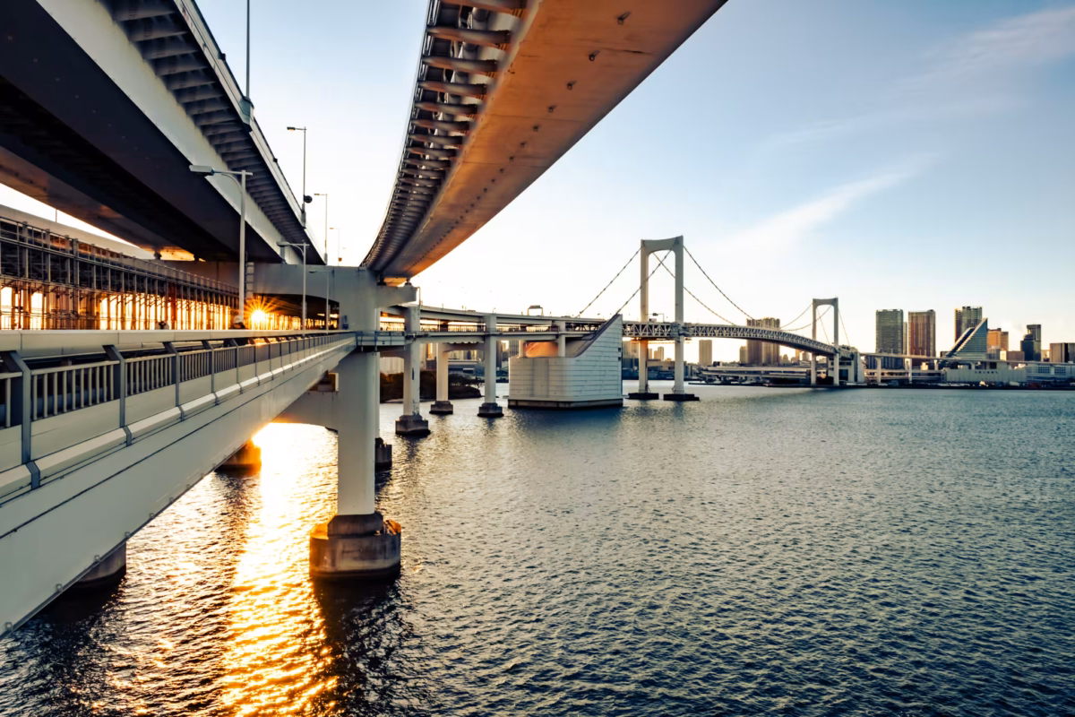 The sun shines through the mesh of a large suspension bridge.