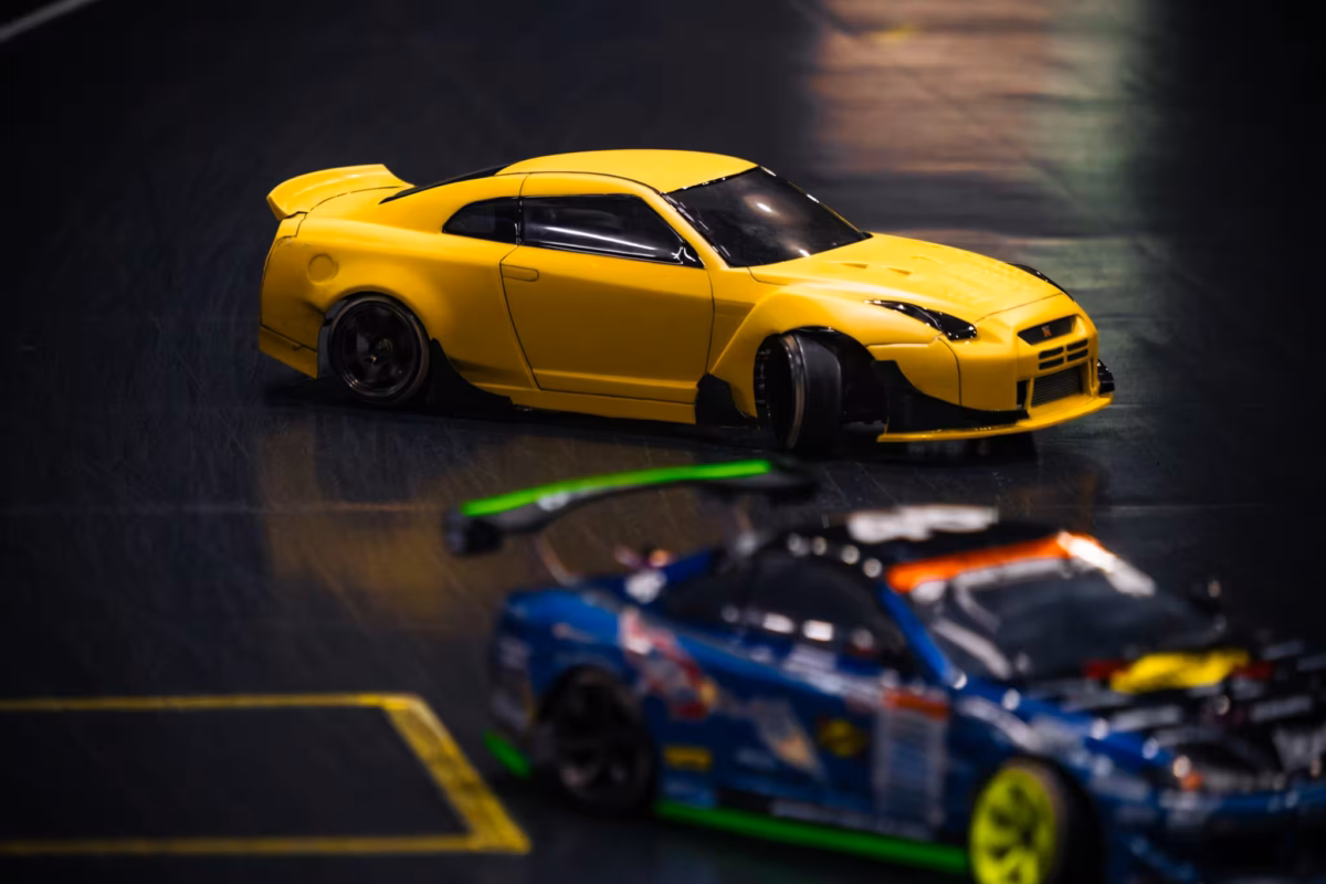 Two RC cars drift into the corner of an indoor track.