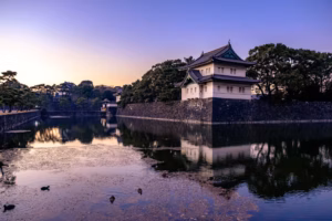 A Japanese traditional castle turret next to a moat at sunset.