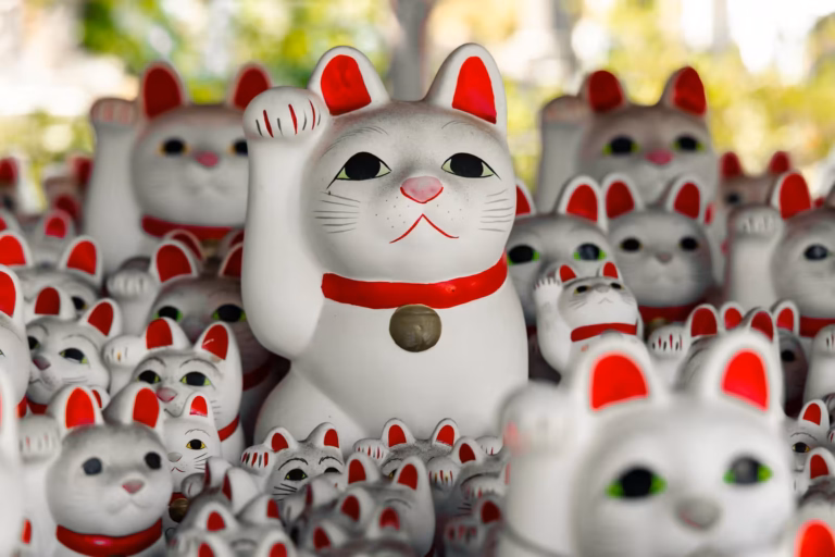 A central white Maneki-neko figurine surrounded by many others at Gotokuji Temple, with a soft-focus background.