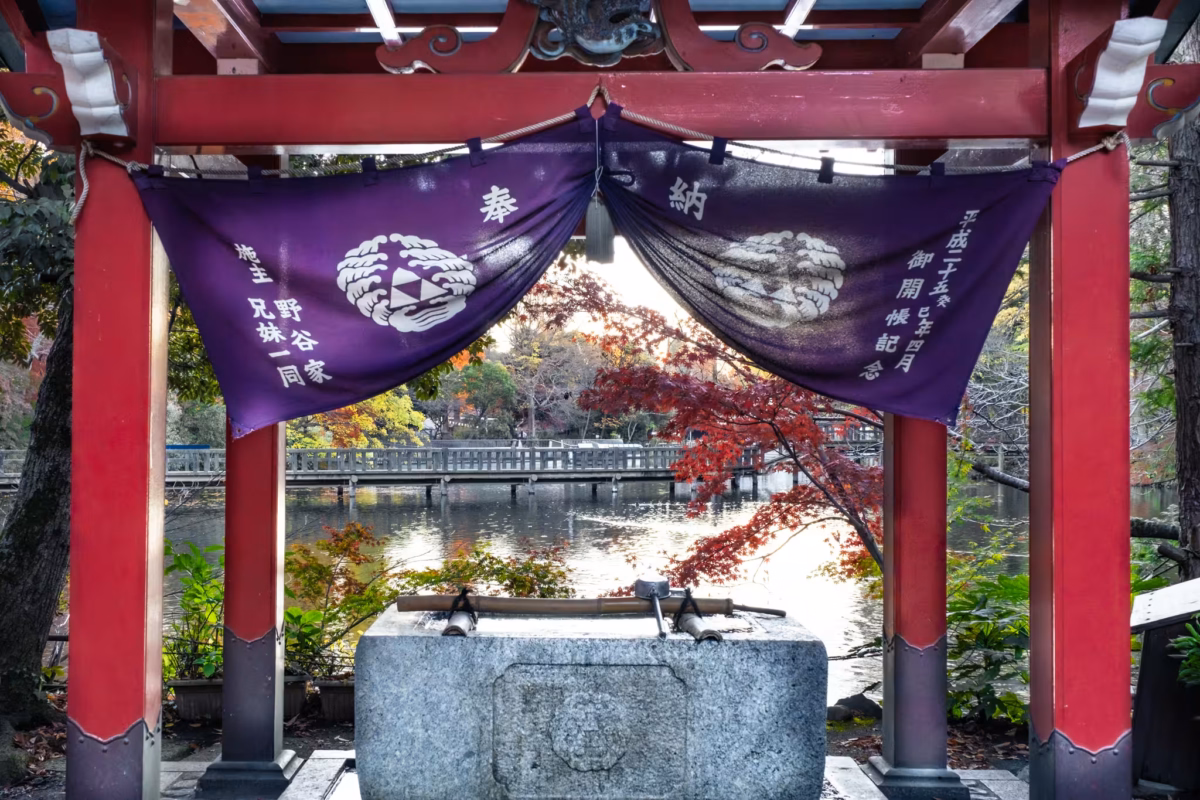 A temple wash basin under a roof sits next to a pond with a bridge.
