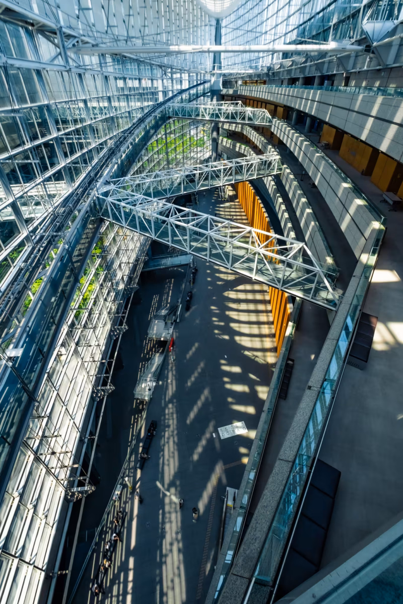 High-angle view of the Tokyo International Forum’s glass atrium with geometric steel walkways and long shadows.