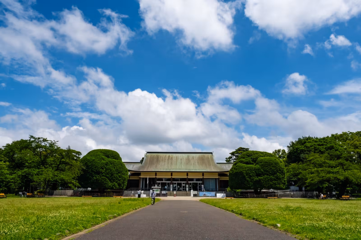Paved path leading to a grand hall at the Edo-Tokyo Open Air Architectural Museum under a vibrant blue sky.