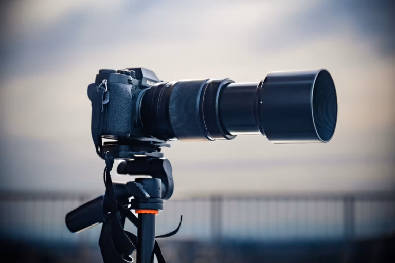 A Fujinon XF55-200mm f/3.5-4.8 attached to an X-T2 sits upon a tripod against a blurred background.