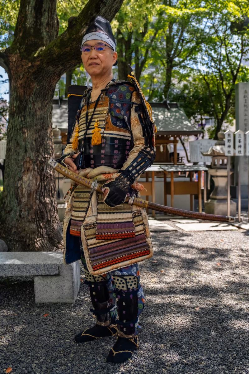 A Heian-period samurai reenactor stands under a shady tree.