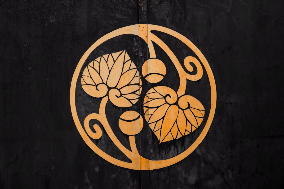 A gold Futaba-aoi (double-hollyhock) crest on a dark, weathered background at Hie Shrine in Tokyo.