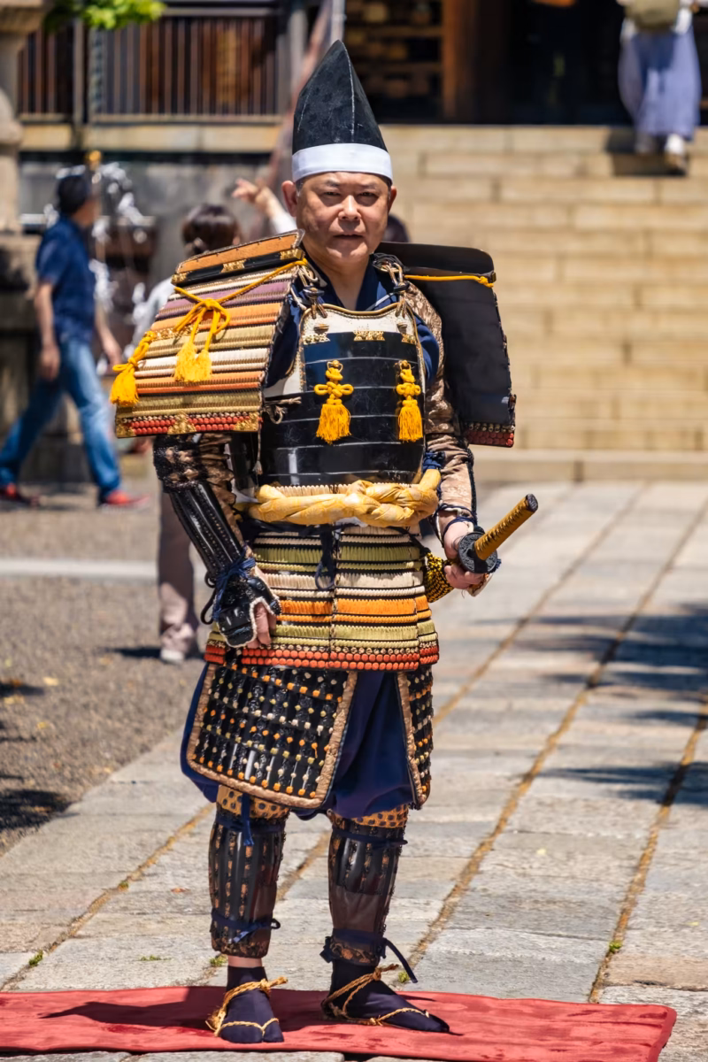 A Heian-period samurai reenactor in armor holds a sword at his side in his left hand.