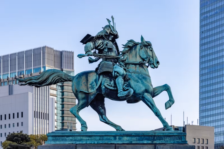 Bronze equestrian statue of Kusunoki Masashige on a rearing horse, set against modern city skyscrapers.