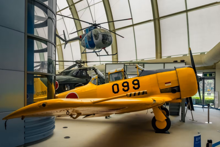 Bright yellow North American T-6 Texan trainer aircraft and a suspended blue helicopter in an aviation museum.