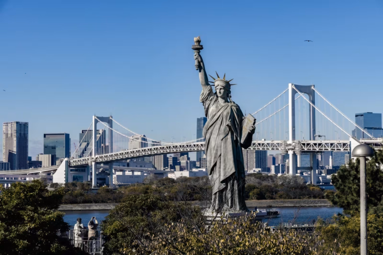 Statue of Liberty replica in Odaiba, Tokyo, with the Rainbow Bridge and city skyline in the background under a blue sky.