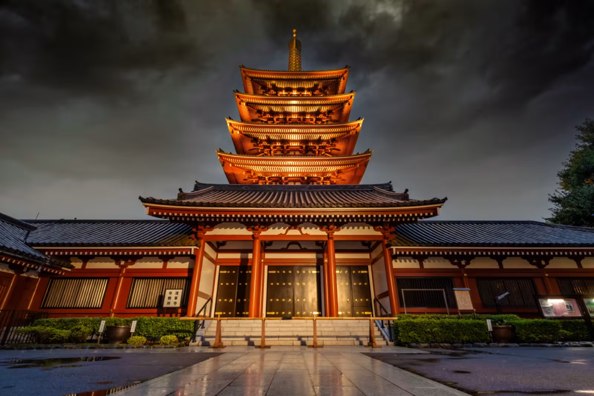 The illuminated Hozomon Gate at Senso-ji Temple, Tokyo, at night under a dramatic, dark cloudy sky.
