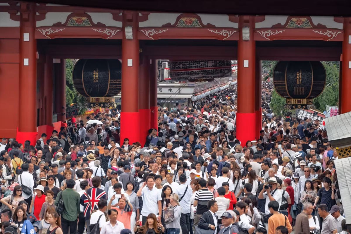 Massive crowd walking through the red Hozomon Gate at Senso-ji Temple in Asakusa, Tokyo, under large black lanterns.