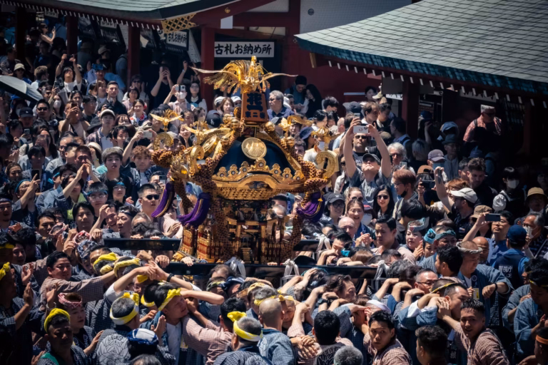 A dense crowd of participants carries a golden mikoshi shrine during Tokyo's energetic Sanja Festival.