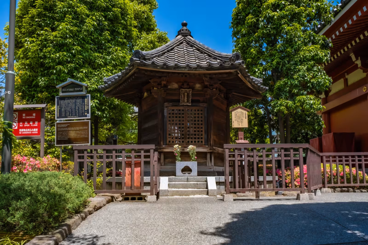 The historic wooden Hexagonal Temple at Senso-ji in Tokyo, surrounded by lush green trees on a bright day.