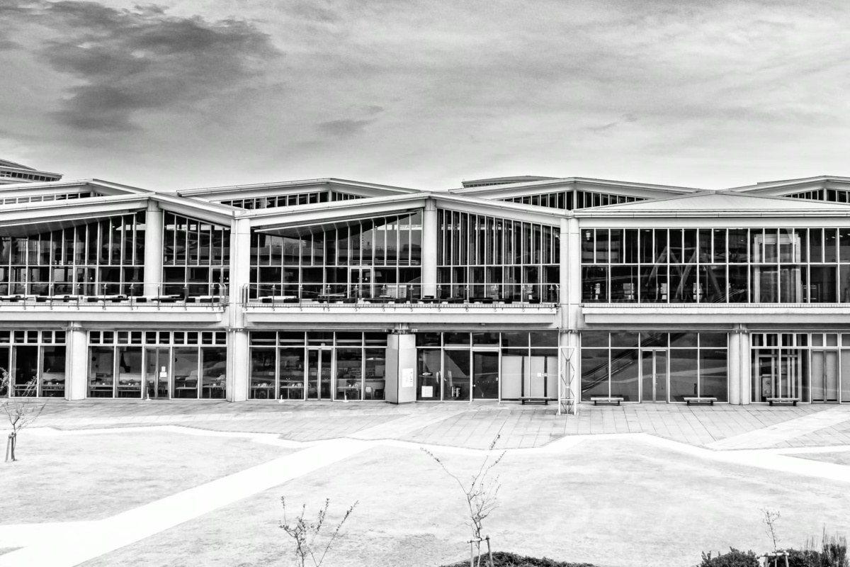 B&W architectural view of the repetitive glass facade and zig-zag roofline of the Tokyo Big Sight exhibition halls.