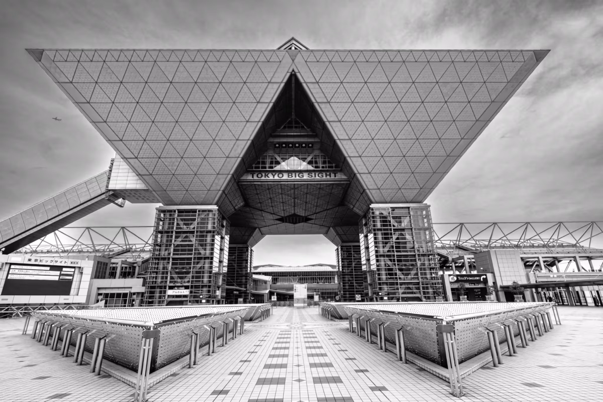 Dramatic B&W wide shot of the Tokyo Big Sight Conference Tower soaring above a symmetrical tiled plaza.