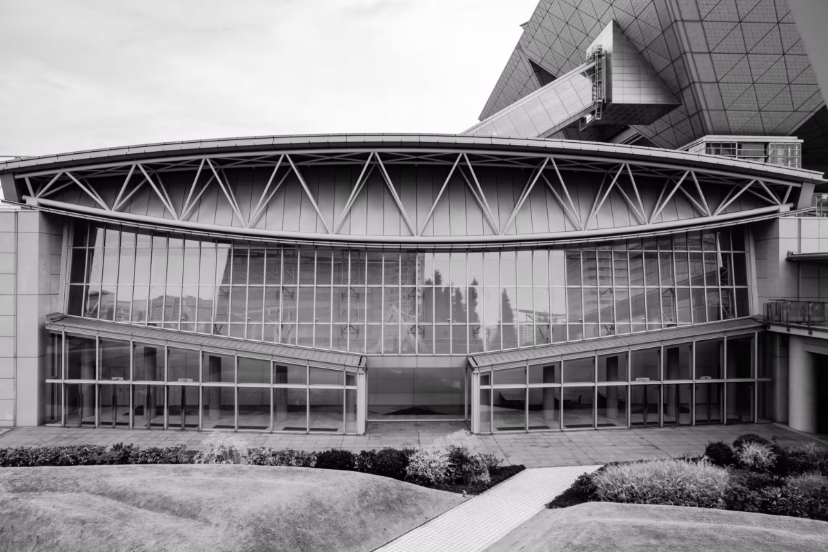 B&W architectural view of a curved glass hall at Tokyo Big Sight with landscaped garden mounds in the foreground.