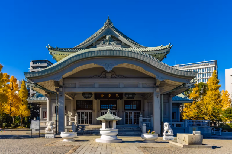 Tokyo Metropolitan Memorial Hall with its iconic curved roof, framed by yellow ginkgo trees under a bright blue sky.
