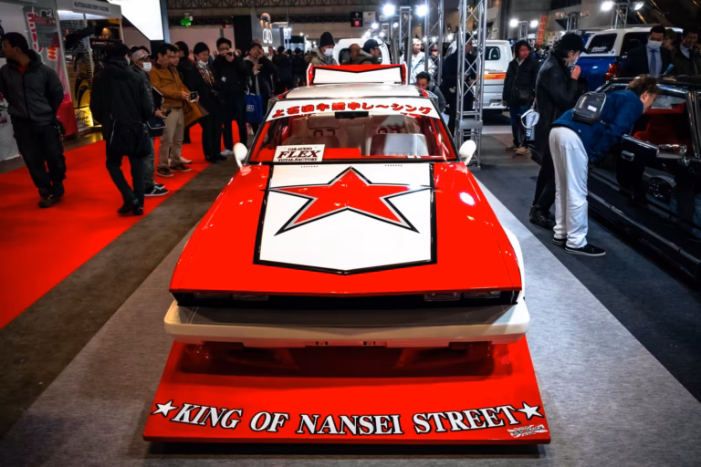 A customized red and white car with a star on the hood and a "King of Nansei Street" splitter at an auto show.