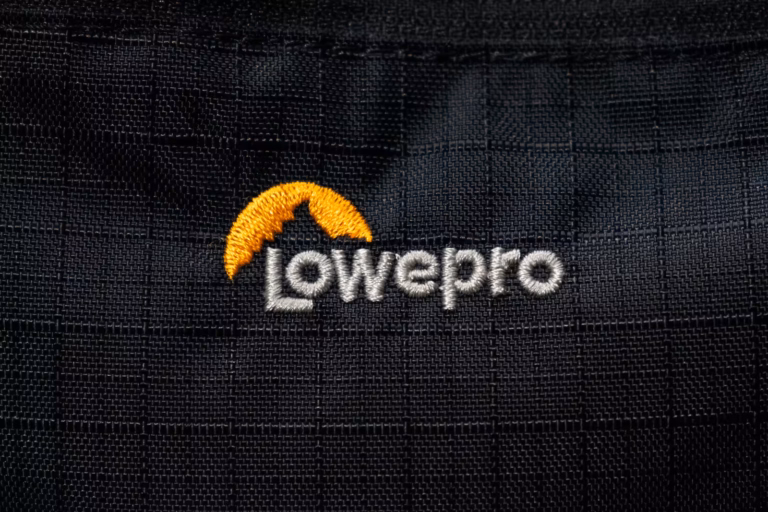 Close-up of the embroidered Lowepro logo on the black fabric of a Lowepro Pro Trekker BP 350 AW II backpack.