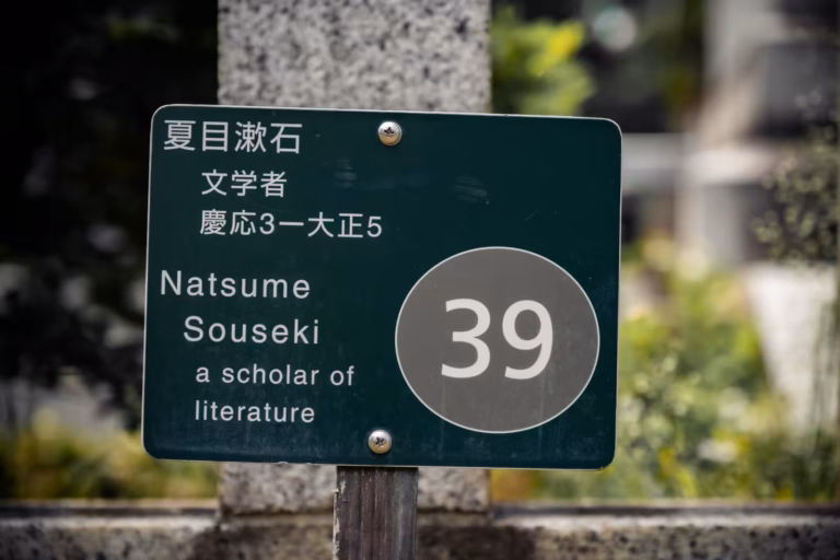 Green plaque marking the grave of scholar Soseki Natsume with Japanese and English text at Zoshigaya Cemetery.