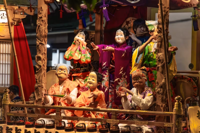 Hyottoko and Okame performers in traditional dress dance on a carved wooden float during the Kurayami Festival.