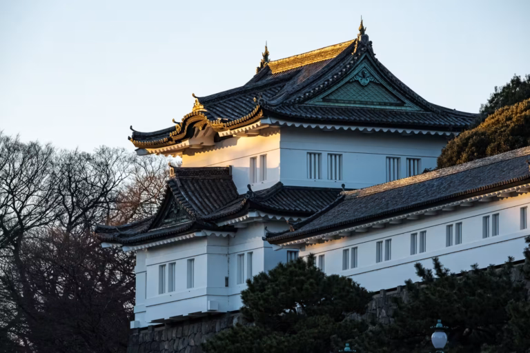 Sunlight illuminates a white watchtower with dark tiered roofs and gold accents at the Imperial Palace.