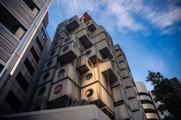 Low-angle shot of Nakagin Capsule Tower's weathered pods with circular windows against a soft twilight sky.