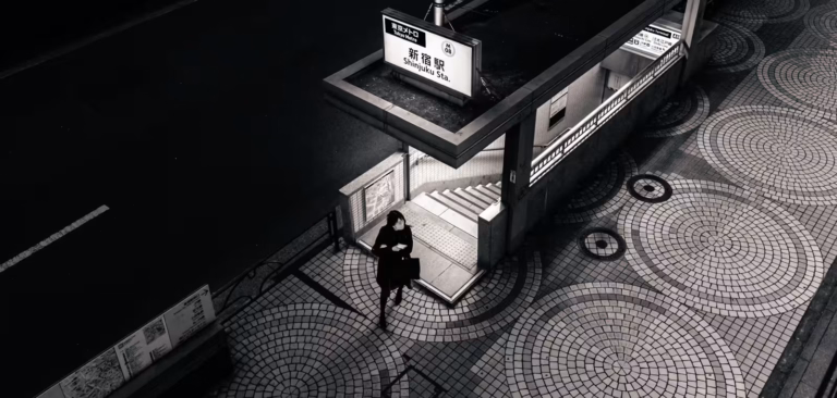 B&W high-angle of a woman at a Shinjuku station. Tokyo’s Mystery Deepens amidst geometric patterns and sharp shadows.