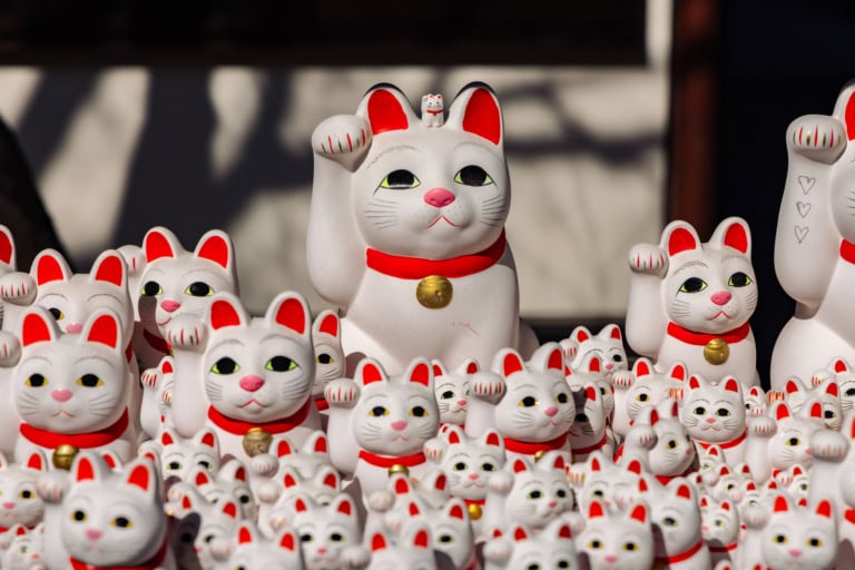 A large Maneki-neko figurine at Gotokuji Temple with a tiny cat on its head, surrounded by many smaller beckoning cats.