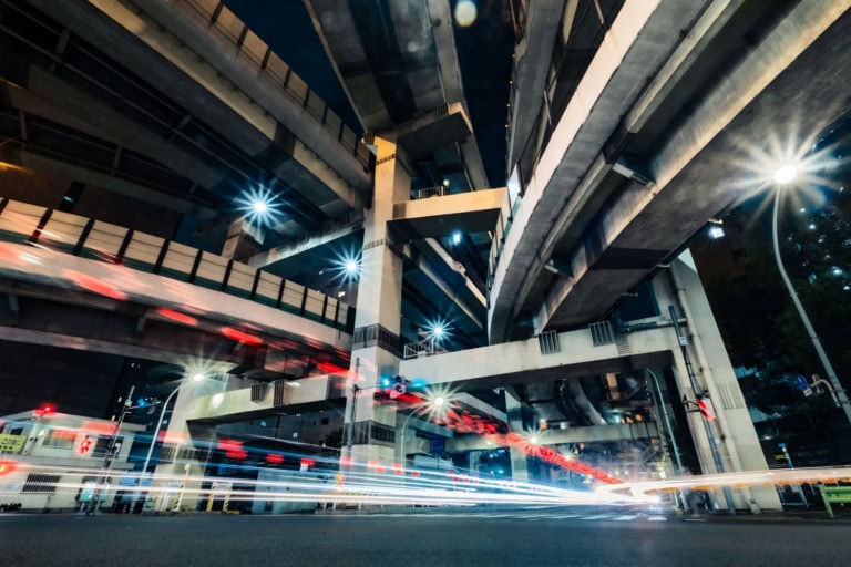 Night long-exposure of Hakozaki Junction featuring light trails beneath complex, towering highway overpasses.