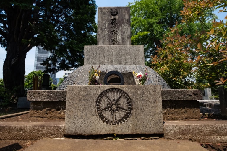 Stone grave of Hideki Tojo with a carved wheel emblem, pebble mound, and tall headstone in a Japanese cemetery.
