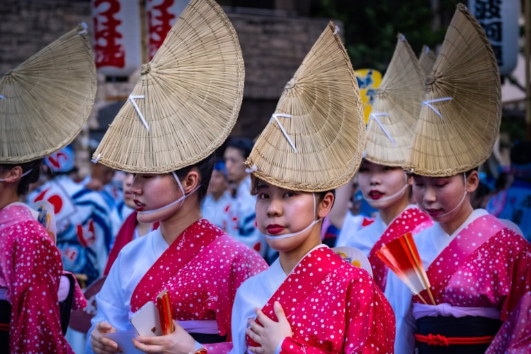 Awa Odori dancers wearing pink polka-dot yukata and tall amigasa straw hats at a Japanese street festival.