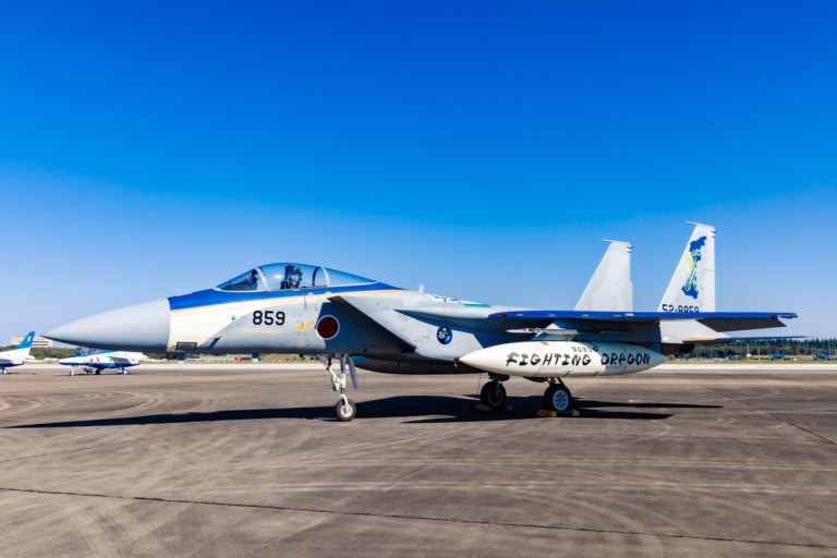 A Mitsubishi F-15J Eagle jet with "Fighting Dragon" fuel tanks at Iruma Air Show 2024 on a sunny tarmac.