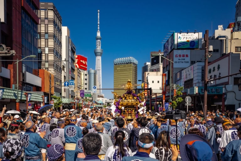 Crowds in traditional dress carry a golden mikoshi toward the Tokyo Skytree during the Sanja Matsuri.