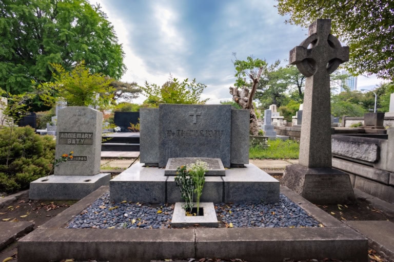 Thomas Baty family graves at Aoyama Cemetery, featuring a large grey stone monument and a Celtic cross under a cloudy sky.