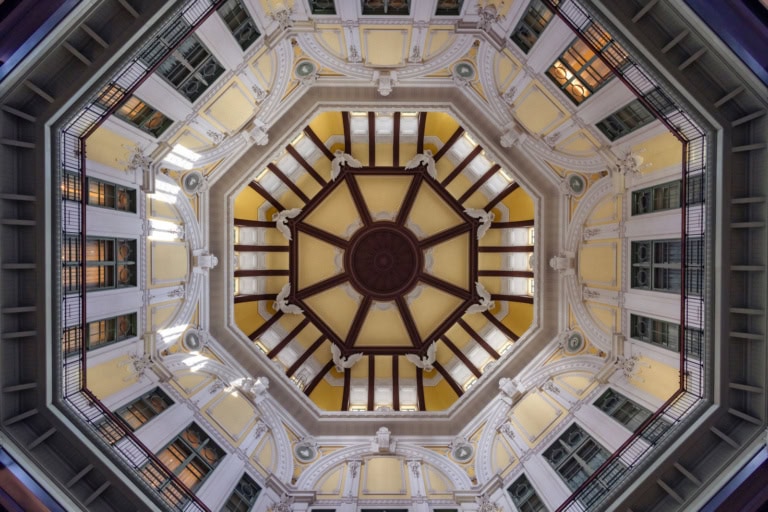 Symmetrical upward view of a yellow octagonal dome with brown ribs, white eagle statues, and architectural tiers.