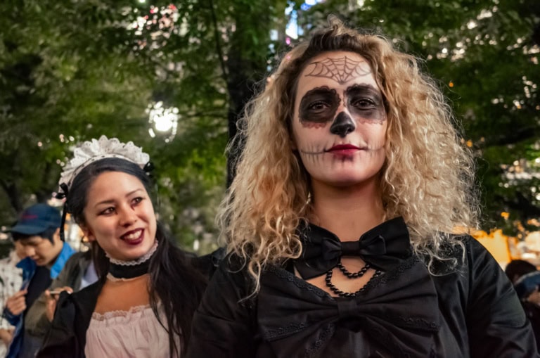 Woman in skeletal face paint and a friend in a maid costume celebrate Shibuya Halloween under city lights.
